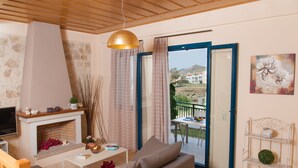 A living room with a fireplace, sofa, coffee table, and a balcony with a view of the countryside. - Villa Peonia & Villa Ortansia (Mylopotamos)