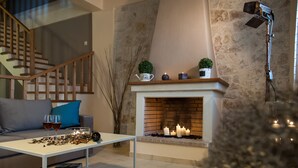 A modern living room with a fireplace, a staircase, and a coffee table with books and glasses. - Villa Peonia & Villa Ortansia (Mylopotamos)
