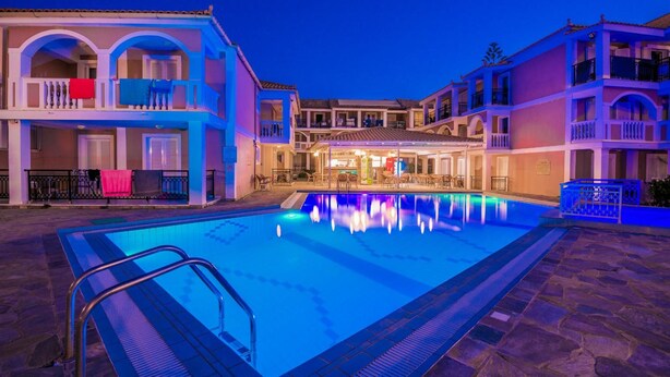 Ein Swimmingpool mit glatter, blauer Wasseroberfläche, umgeben von Gebäuden mit Balkonen und einer überdachten Außenbereich-Sitzgelegenheit.