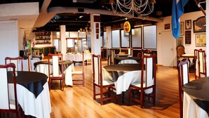 A restaurant interior with multiple tables and chairs, wooden flooring, and wall decorations including framed pictures and a Coca-Cola sign. - Atlantida Hotel (Río Grande)