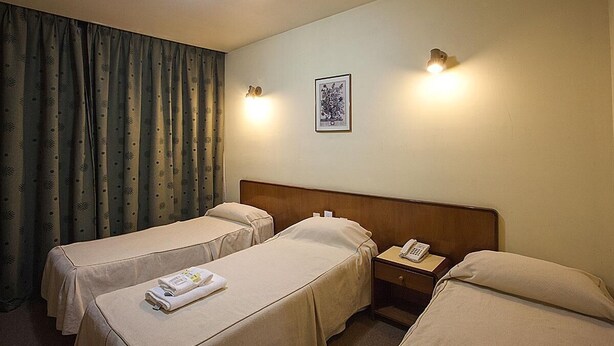 A hotel room with two single beds, a bedside table with a telephone, a wall-mounted light, and a framed picture. - Atlantida Hotel (Río Grande)