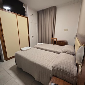Habitación de hotel con dos camas, un armario, un escritorio y una silla.