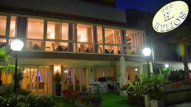 A hotel with a double-story structure, large windows, and a well-lit entrance. - Helios (Cervia)