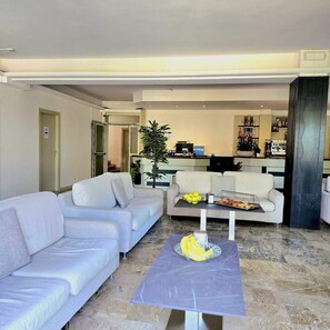 Un salón moderno con un sofá, una mesa de centro con fruta y una cocina al fondo.