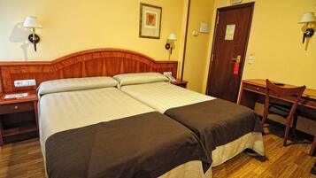 A double bed with a wooden headboard, two bedside tables with lamps, a desk with a chair, and a door with a sign.