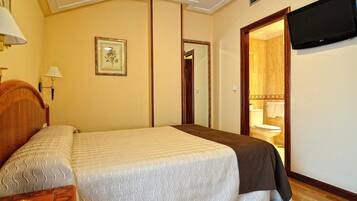 A hotel room with a bed, a bedside table, a lamp, a framed picture on the wall, a television mounted on the wall, and a door leading to a bathroom.