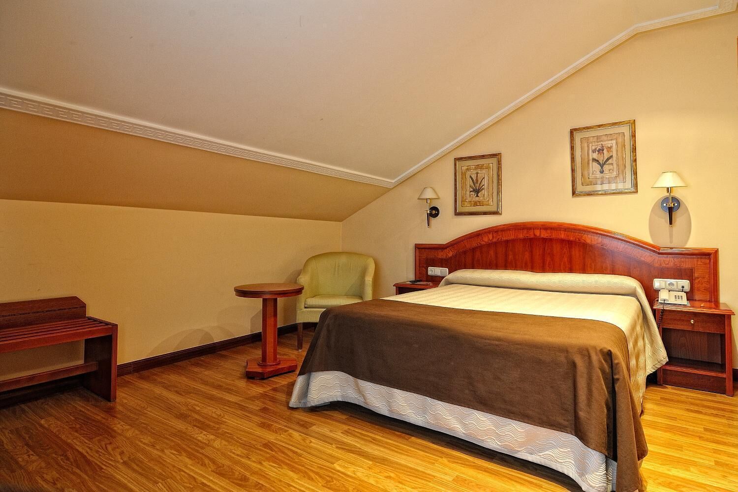 Una habitación de hotel con una cama de madera, una silla, una mesita pequeña y una mesita de noche.
