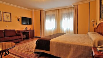 A hotel room with a bed, a sofa, a desk, a television, and a window with curtains.