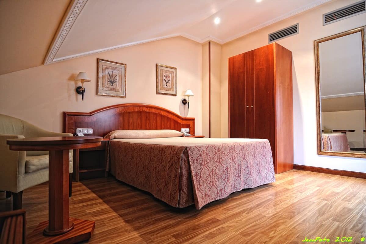 Habitación de hotel con cama de madera, mesita de noche, una mesa y un armario.