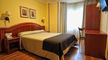 Una habitación de hotel con una cama de madera, dos lámparas de noche, un escritorio con televisor y dos cuadros en la pared.