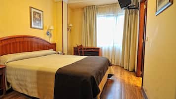 A hotel room with a large bed, a desk, a chair, a television, and a window with curtains.