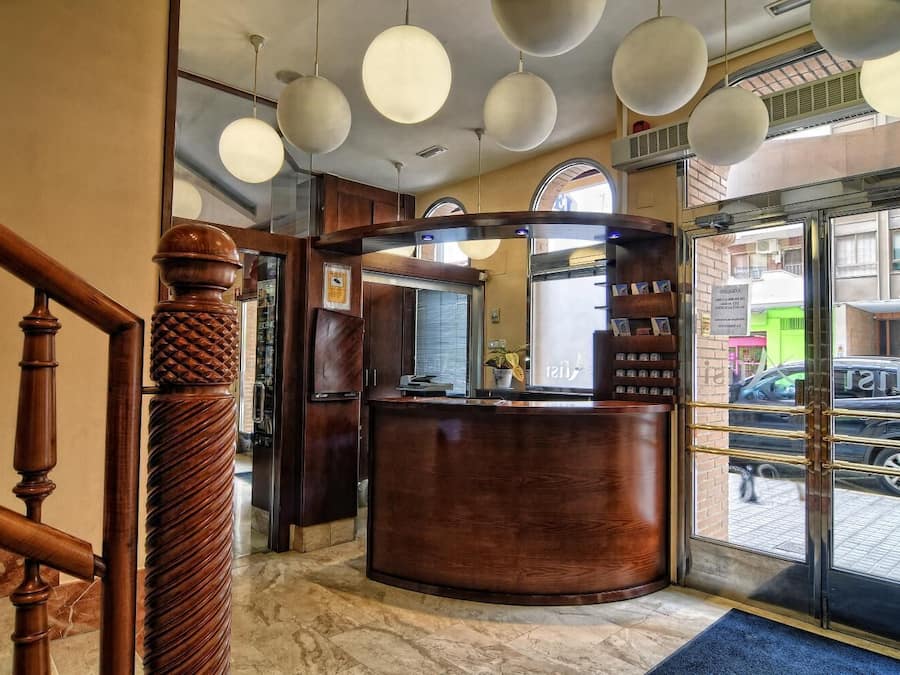 Una recepción con mostrador de madera, suelo de mármol y puerta de cristal que da al exterior.