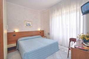 Habitación de hotel con cama, mesita de noche, lámpara, silla, escritorio y televisor.