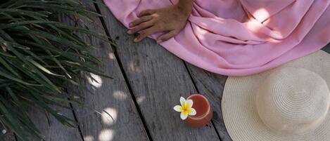 Una terraza de madera con tela rosa, un sombrero de paja y una maceta pequeña con una flor.