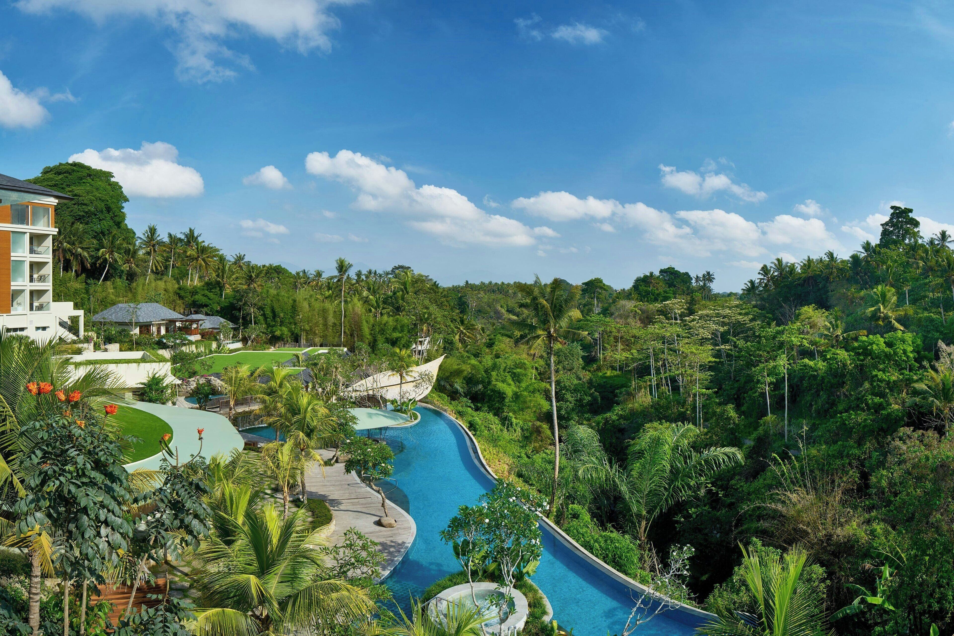 A resort with a winding pool, lush greenery, and a modern building with balconies.