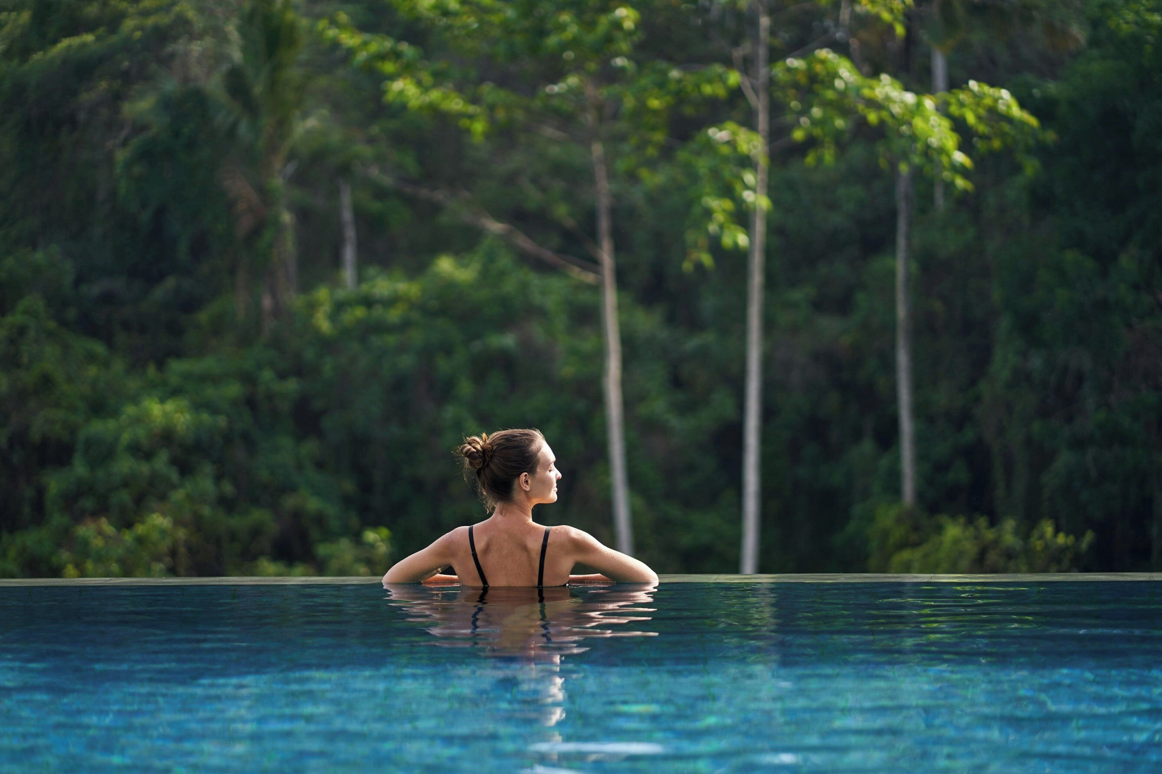 A person in a swimming pool with a natural, forested background.