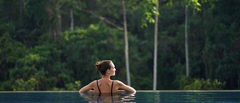 A person in a swimming pool with a natural, forested background.