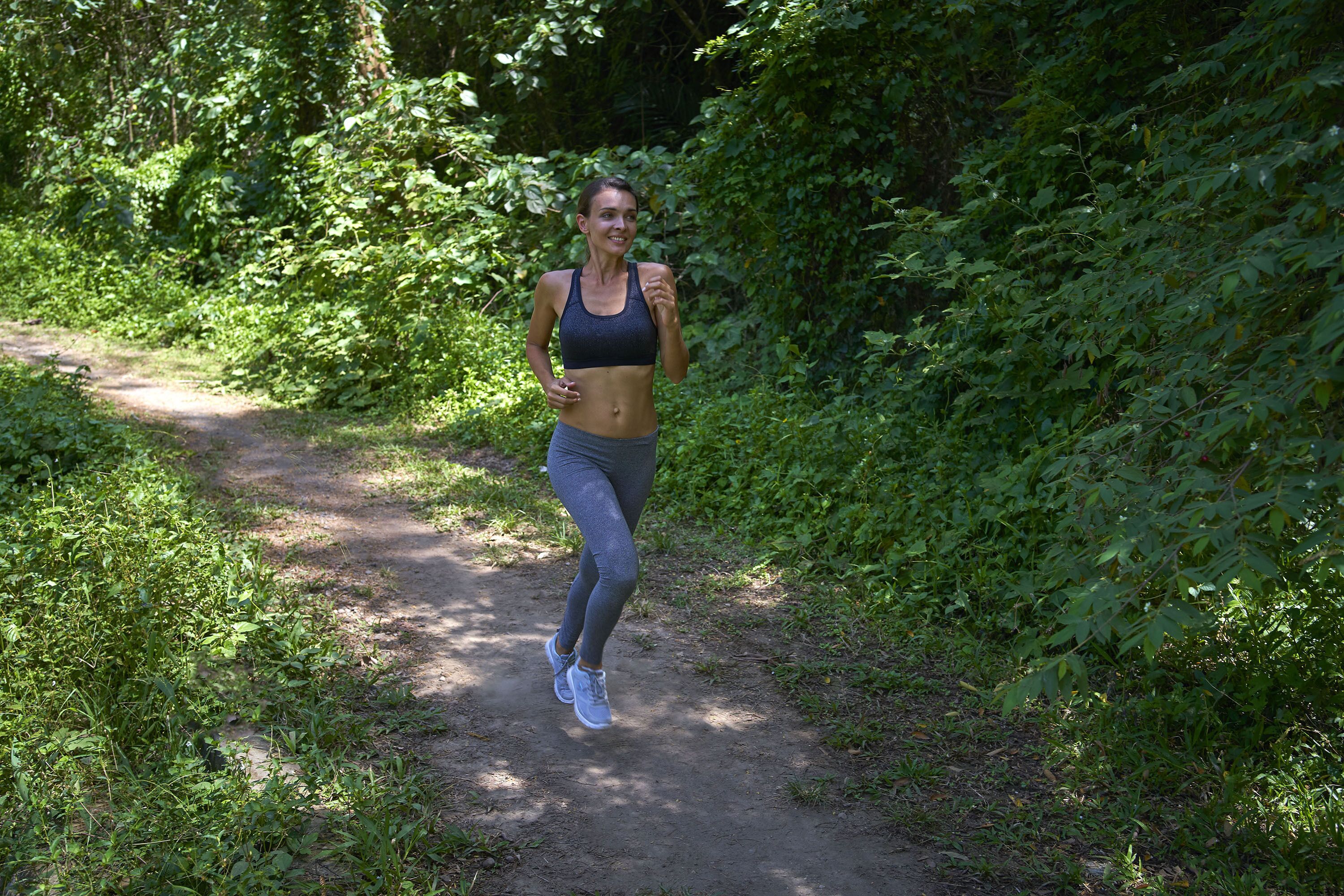 A person jogging on a dirt path surrounded by dense greenery.