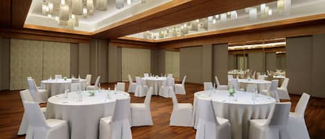 Un salón de conferencias con varias mesas redondas, sillas blancas e iluminación colgante moderna.