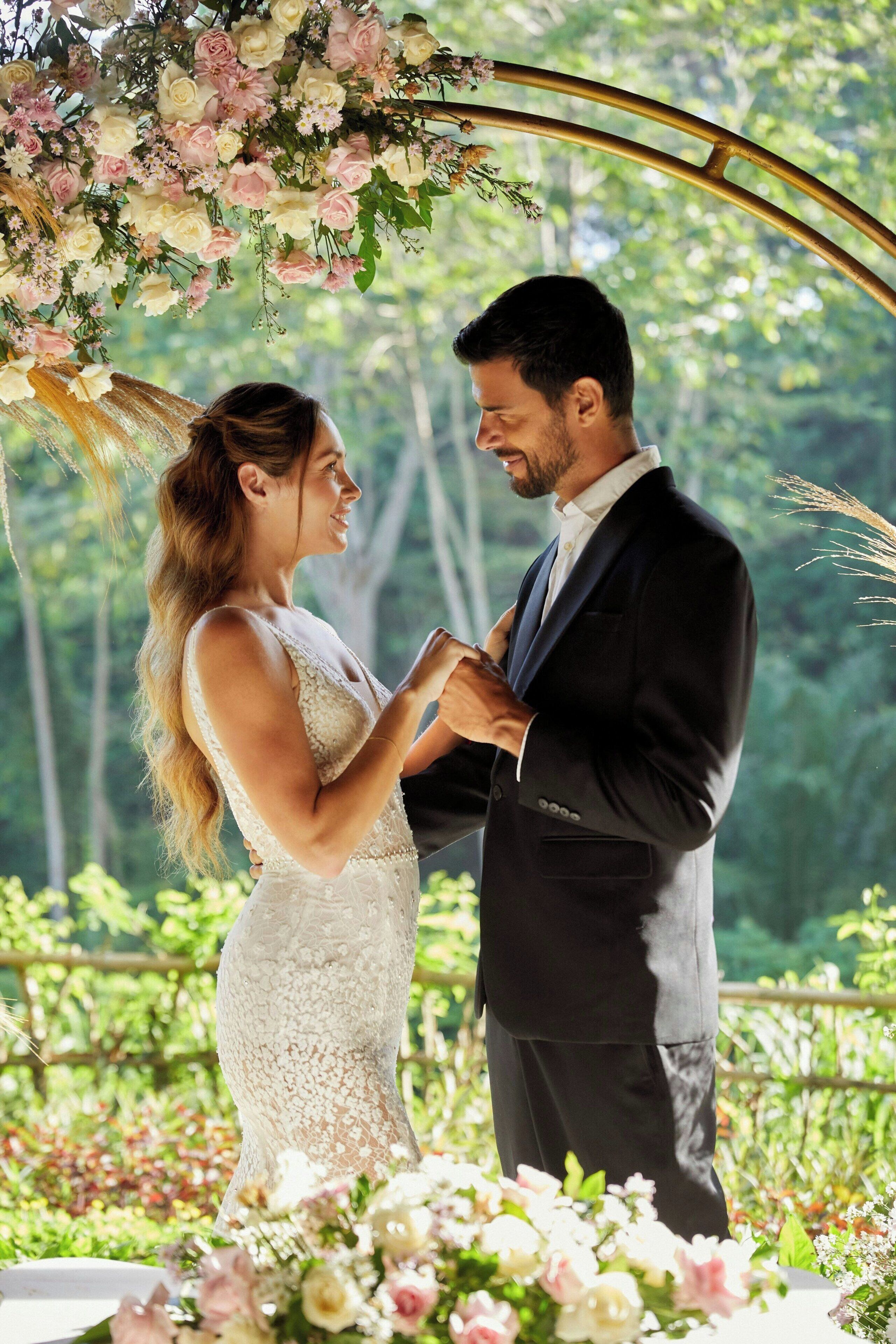 Un couple se tient sous une arche fleurie, dans un jardin.
