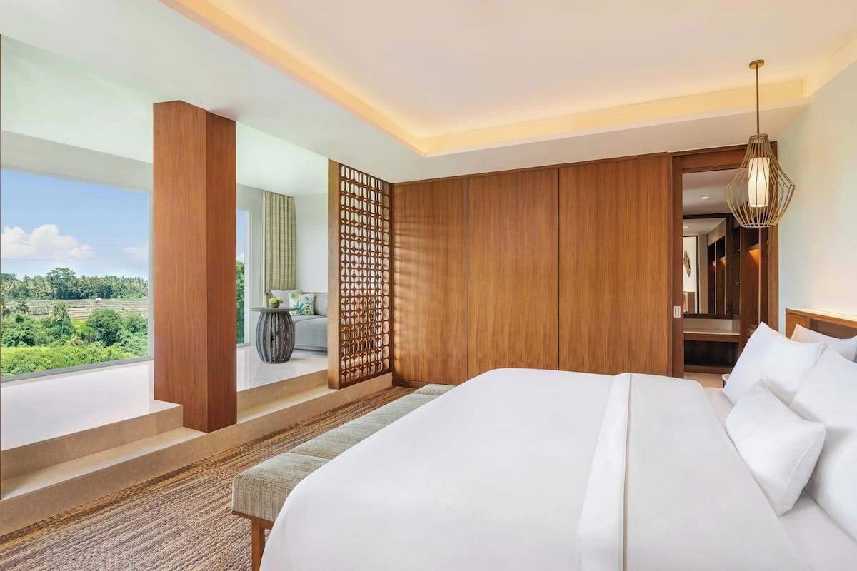A modern hotel room with a large bed, wooden paneling, a view of greenery, and a balcony.