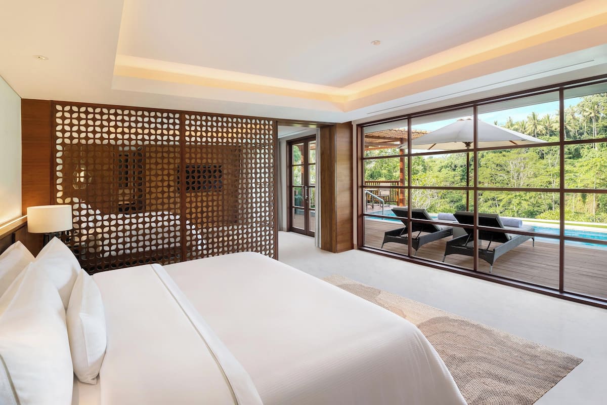 A modern hotel room with a large bed, a wooden partition, and a balcony with a pool view.