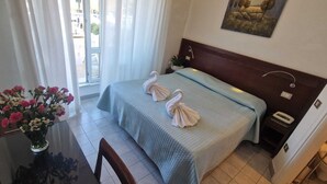 Une chambre d’hôtel avec un lit, une table de chevet, un vase de fleurs et une fenêtre avec des rideaux.