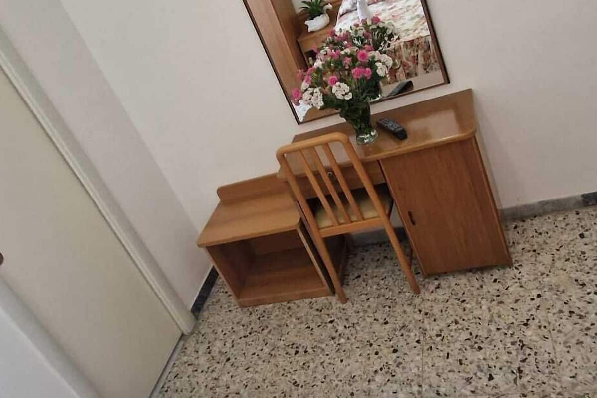 Hotellihuone, jossa on sänky, puinen työpöytä, peili ja seinälle asennettu televisio.