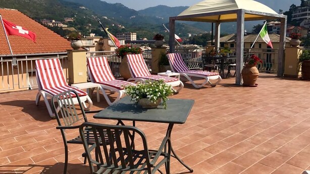 Une terrasse avec des fauteuils de jardin à rayures rouges et blanches, une table ornée d’une plante en pot et un auvent.