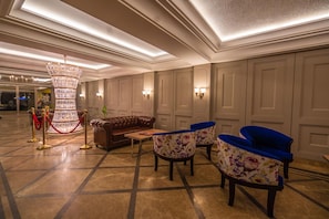 A lobby with a chandelier, leather sofa, floral chairs, and a red rope barrier.