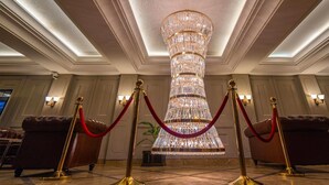 A grand chandelier in a hotel lobby with red velvet ropes and gold stanchions. - Castle Salam (Khulna)