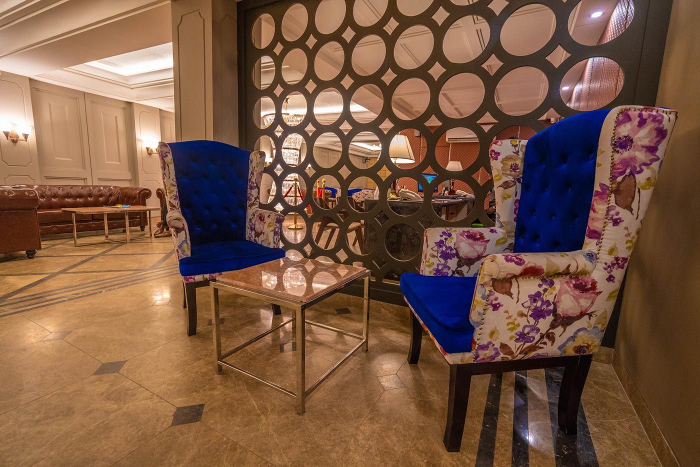 Un vestíbulo con dos sillones tapizados en azul, una mesa de centro de vidrio y una pared decorativa con círculos recortados.