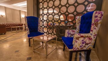 A lobby with two blue upholstered chairs, a glass coffee table, and a decorative wall with circular cutouts.
