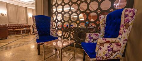 Un vestíbulo con dos sillones tapizados en azul, una mesa de centro de vidrio y una pared decorativa con círculos recortados.