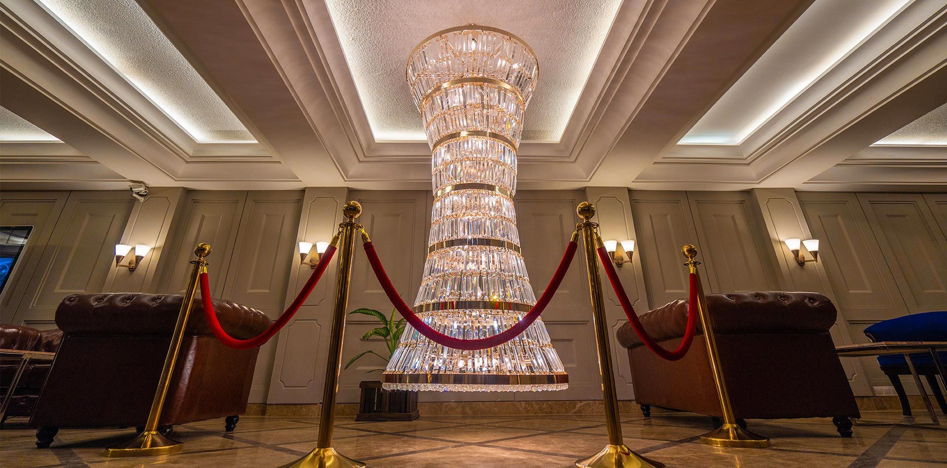 A grand chandelier in a hotel lobby with red velvet ropes and gold stanchions.