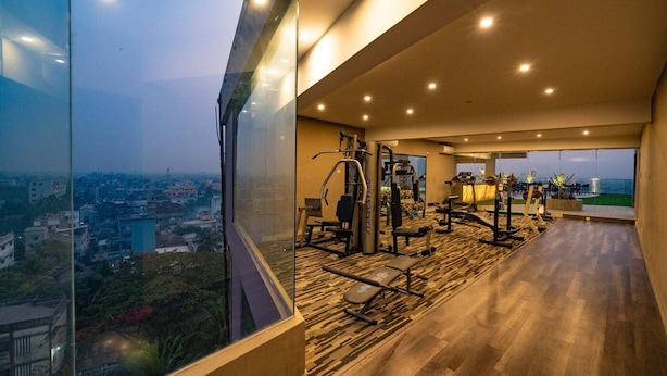 A gym with exercise equipment and a large window overlooking a cityscape. - Castle Salam (Khulna)