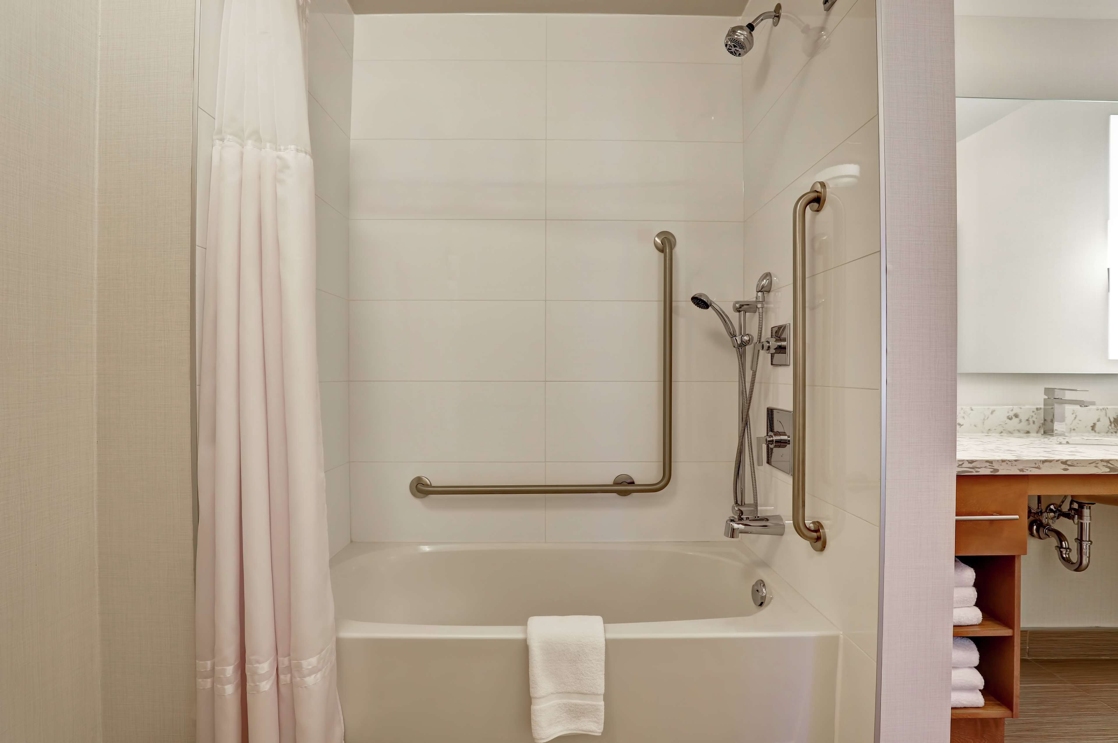 Een moderne badkamer met een bad, handgrepen en een douchegedeelte.