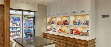 Una suite de hotel con kitchenette, minibar y repisas repletas de bocadillos y bebidas.