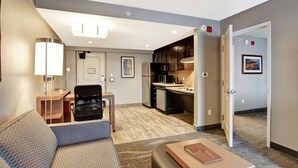 Una habitación de hotel moderna con sofá, escritorio, silla, lámpara y kitchenette.