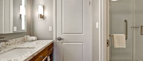 A bathroom with a white door, a glass shower enclosure, and a marble countertop.