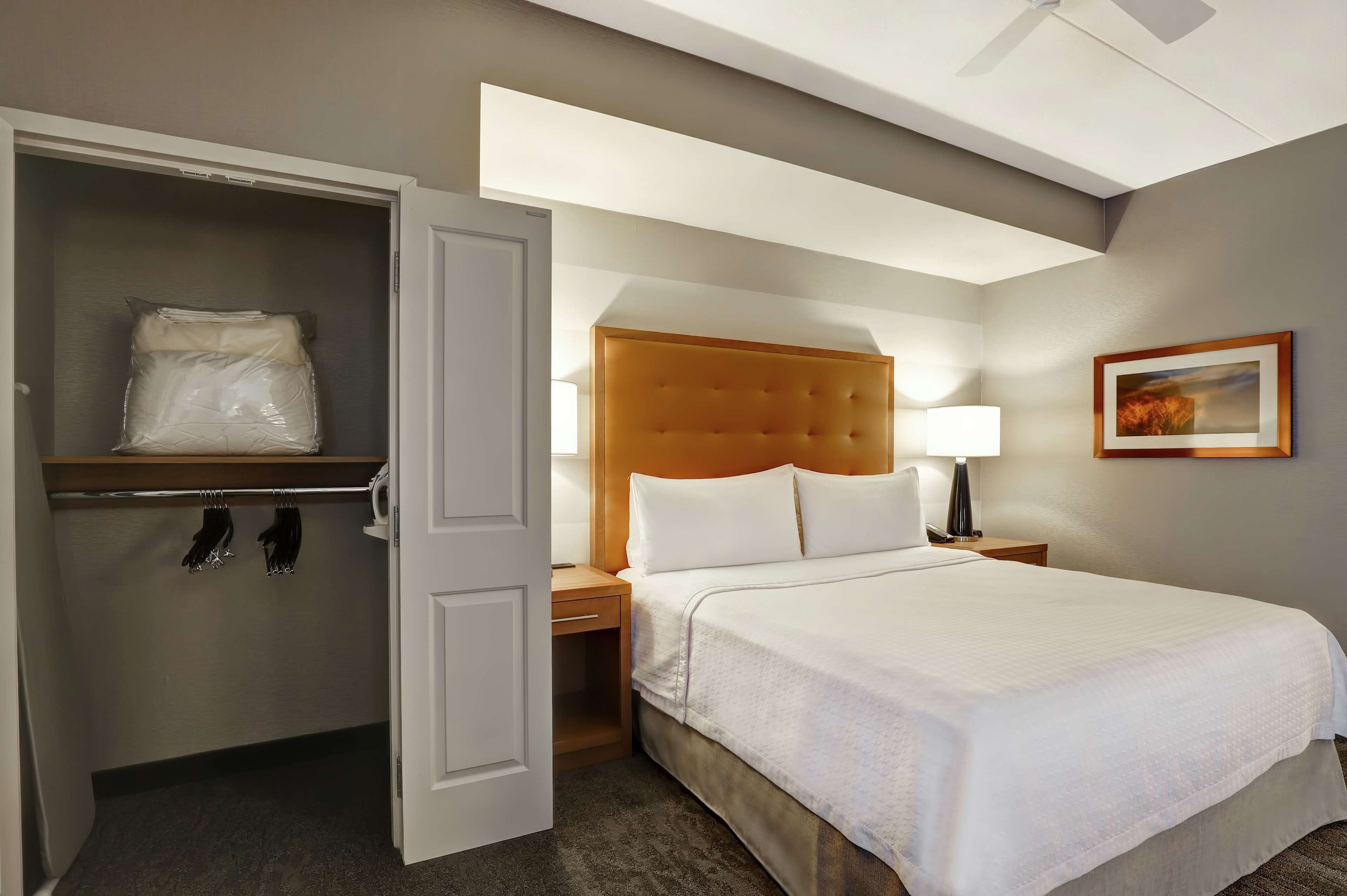 A hotel room with a bed, a nightstand, a lamp, a wardrobe, and a picture on the wall.