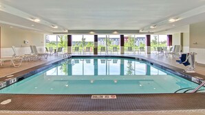 Una piscina interior con agua cristalina, zonas de profundidad señalizadas y sillones de descanso alrededor del borde.