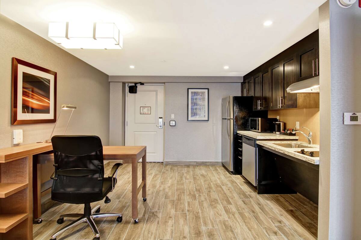 Una cocina moderna con encimera de madera, silla de oficina negra y un refrigerador.