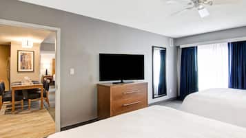Habitación de hotel con cama, televisor en una cómoda de madera, zona de comedor con mesa y sillas, y un ventanal con cortinas.