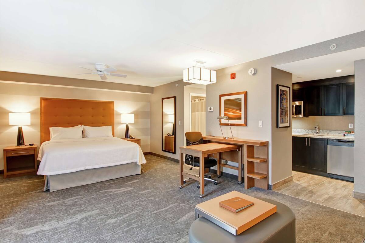 Una habitación de hotel con cama, escritorio, silla y kitchenette.