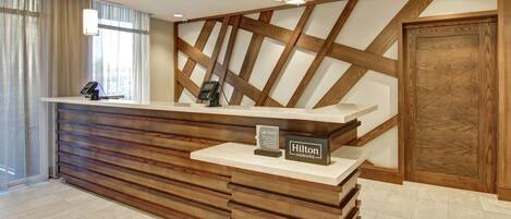 A hotel reception desk with a wooden finish, a white counter, and a sign indicating 'Hilton Honors'.
