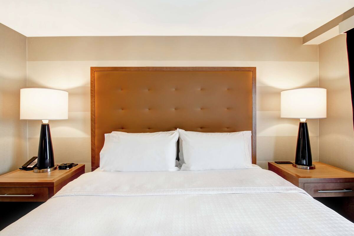 Una habitación de hotel con una cama grande, dos mesitas de noche y dos lámparas.