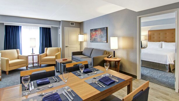 A hotel room with a dining area, two armchairs, a sofa, a bed, and a painting on the wall. - Homewood Suites by Hilton Ottawa Kanata (Ottawa)