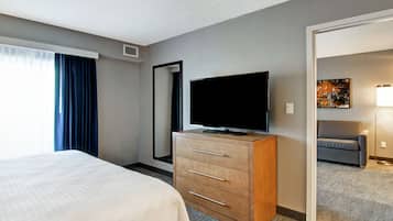 A hotel room with a bed, a TV on a wooden dresser, a large mirror, and a painting on the wall.