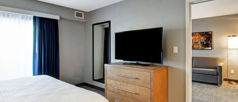 Habitación de hotel con una cama, un televisor sobre una cómoda de madera, un espejo grande y un cuadro en la pared.
